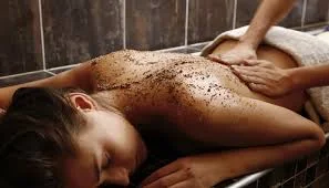 Gommage du dos, grains exfoliants étalés sur la peau d’une cliente allongée