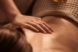 Mains d’une praticienne massant le dos d’une cliente allongée