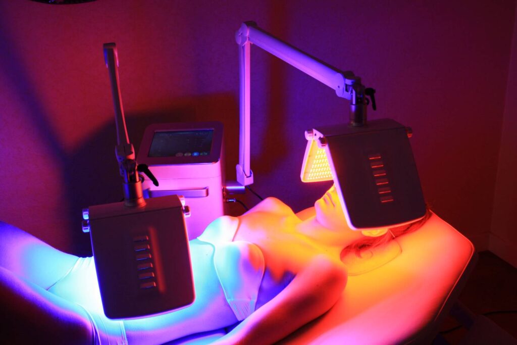 Séance de photomodulation : panneaux de LED rouges et bleues au-dessus du corps d’une cliente allongée